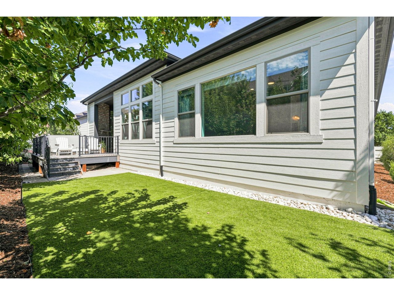 House exterior with large windows, a raised deck, and a tree-shaded lawn.