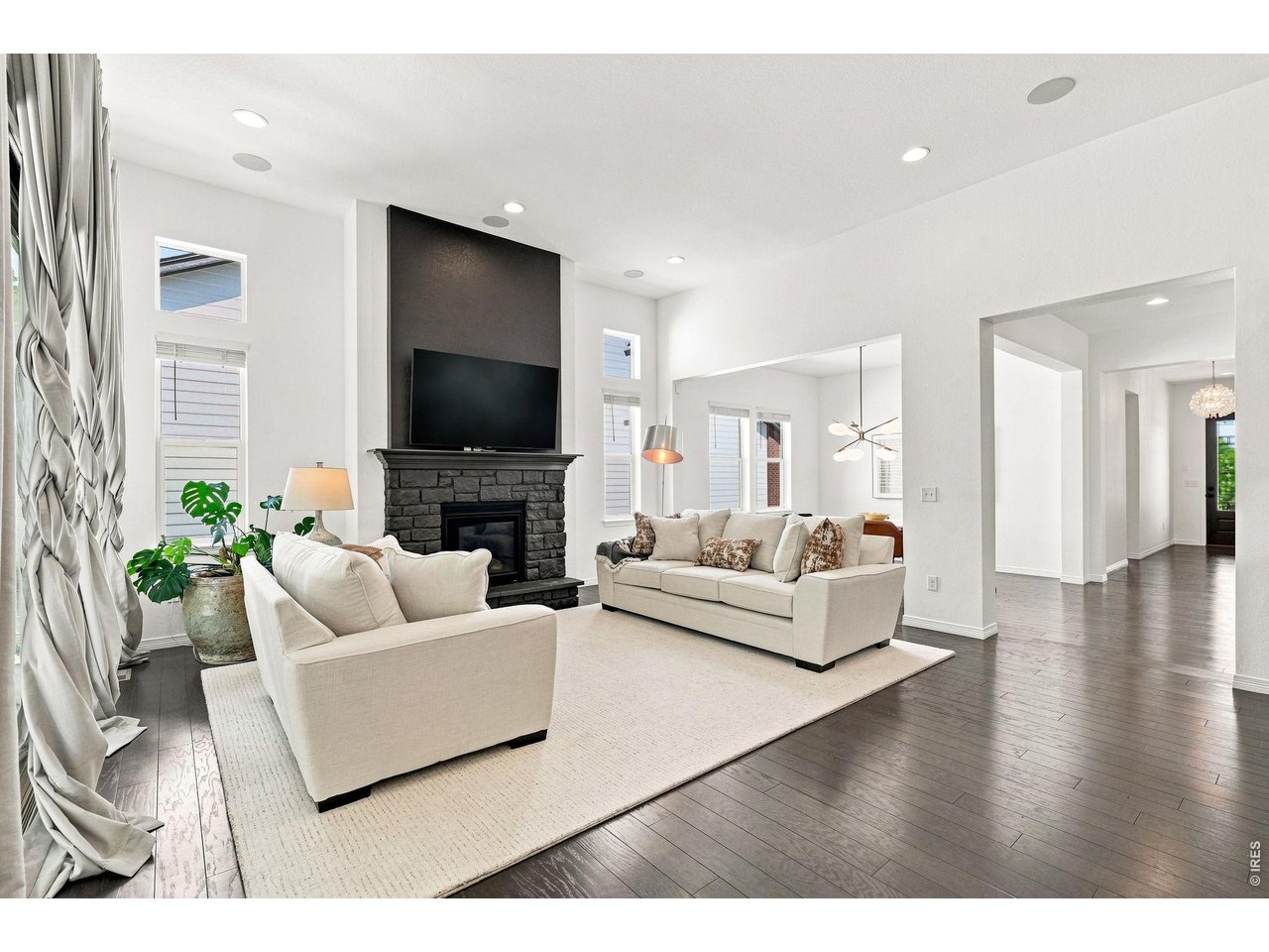 Living room with cream sofas, tall windows, and a dark stone fireplace.