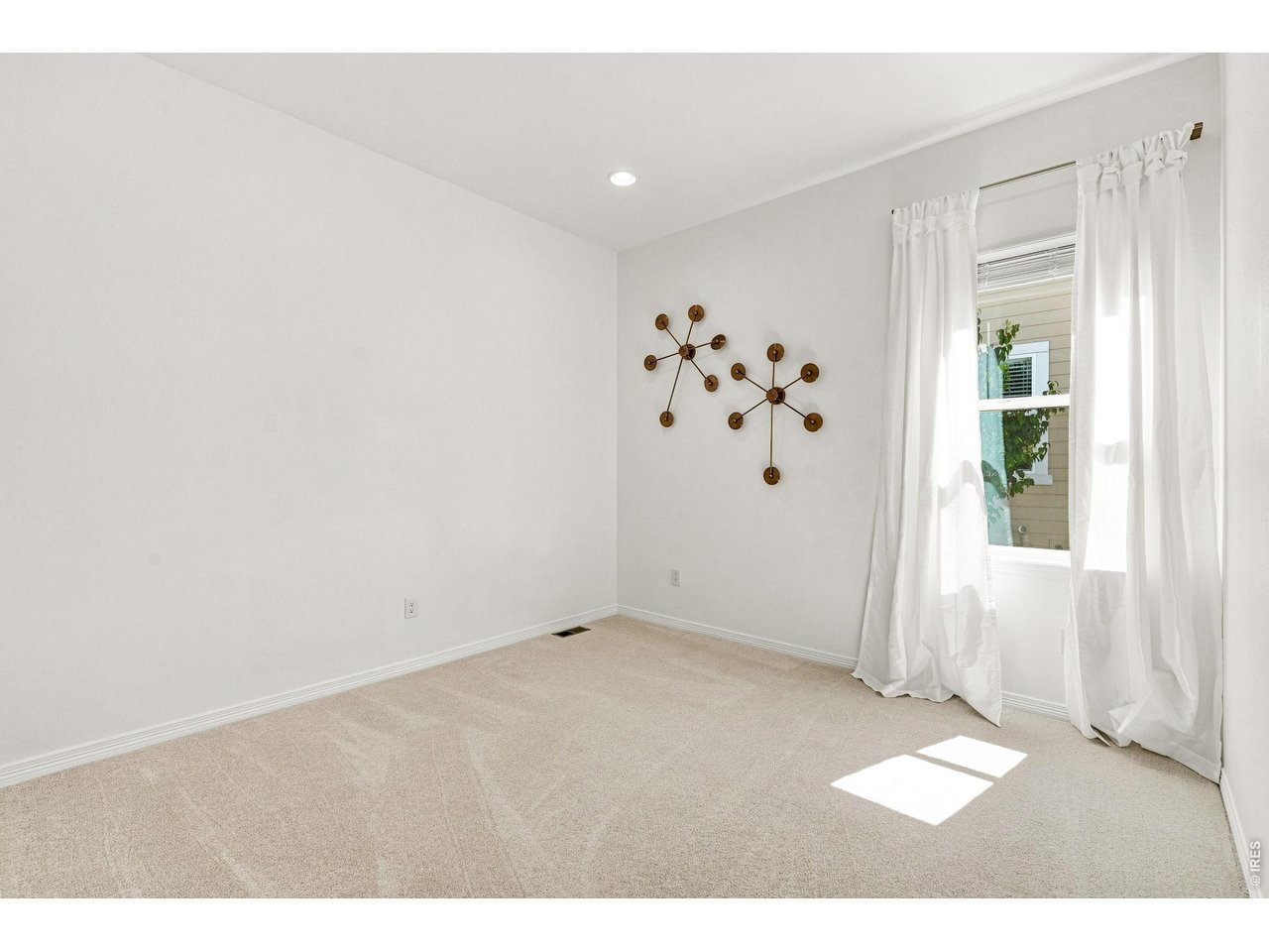 Empty carpeted room with white curtains and bronze starburst wall decorations.