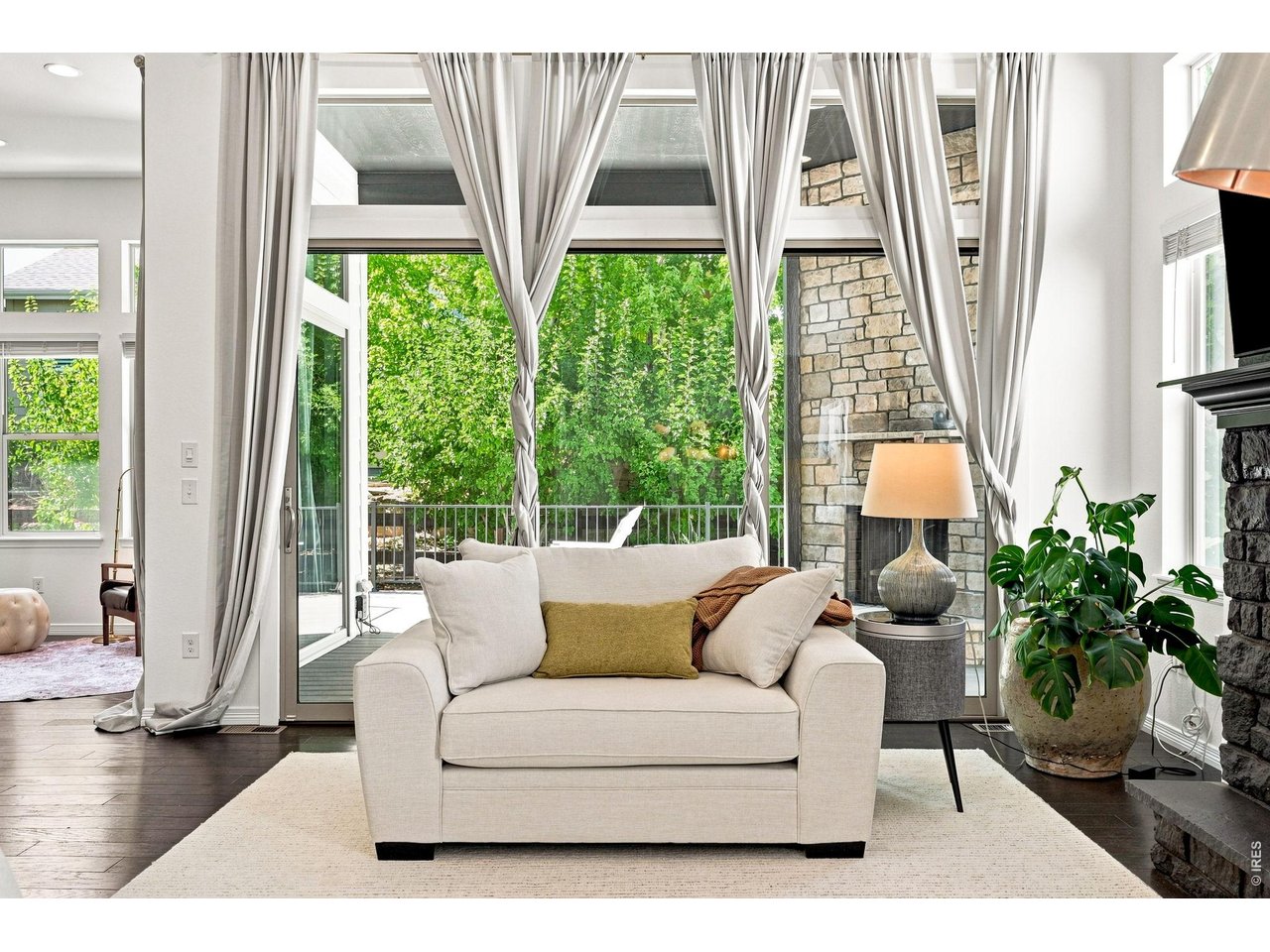 Living room with a cream loveseat, tall curtained windows, and a stone fireplace.