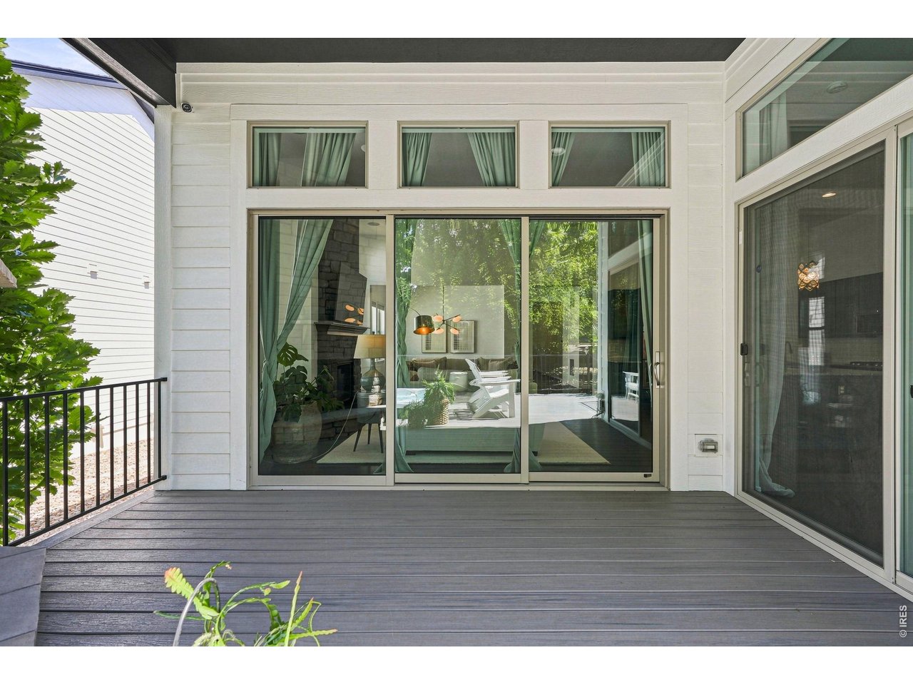 Gray deck outside a white home with large glass doors and a furnished living room beyond.