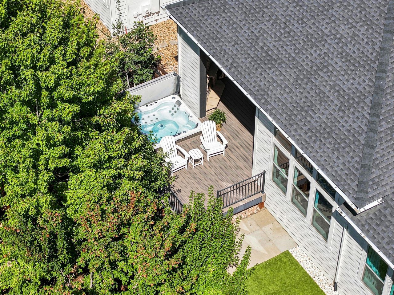 Aerial view of a deck with a hot tub and white Adirondack chairs beside a leafy yard.