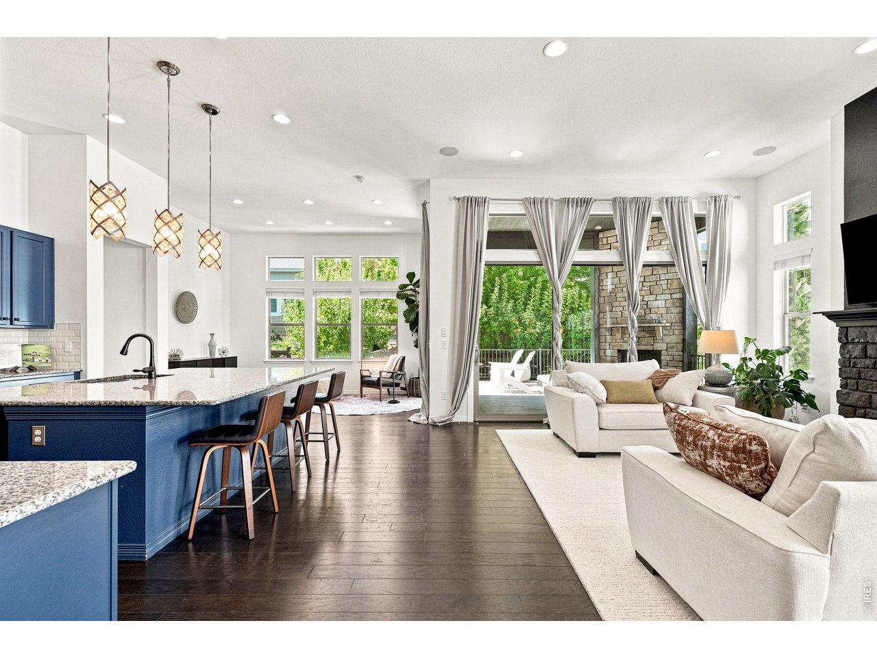 Open-concept kitchen and living room with blue island, white sofas, and stone fireplace.