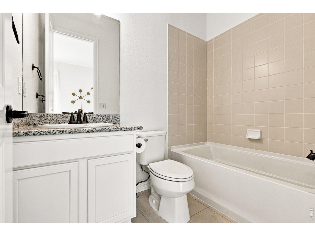 Bathroom with a granite-topped vanity beside a toilet and beige-tiled bathtub.