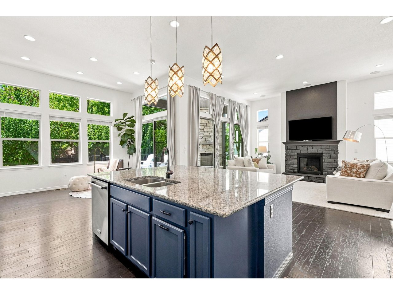 Open-plan kitchen and living room with a blue island, tall windows, and a stone fireplace.