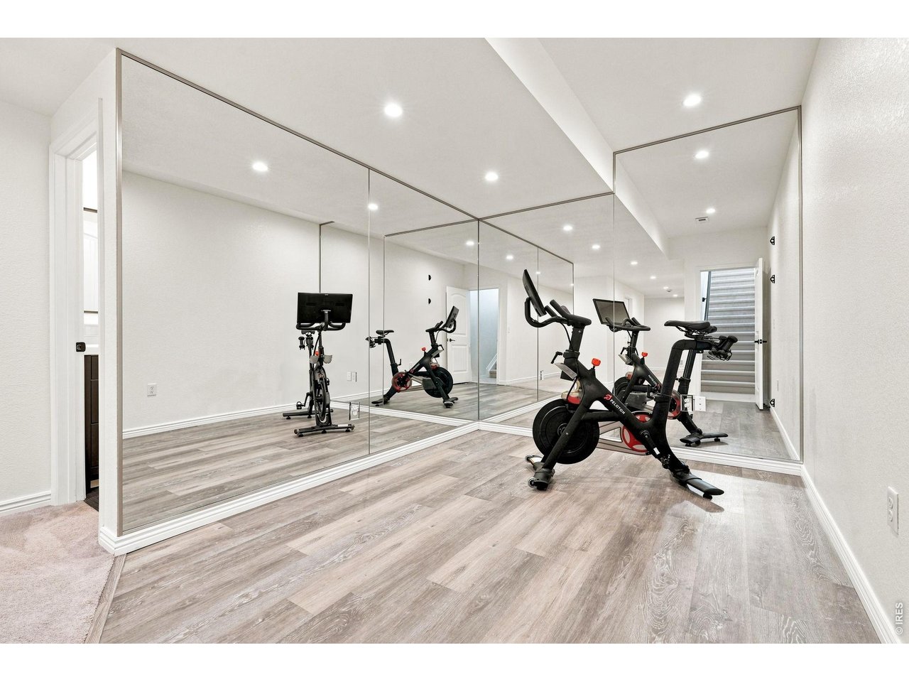 Home gym with mirrored walls, two stationary bikes, and stairs at the back.