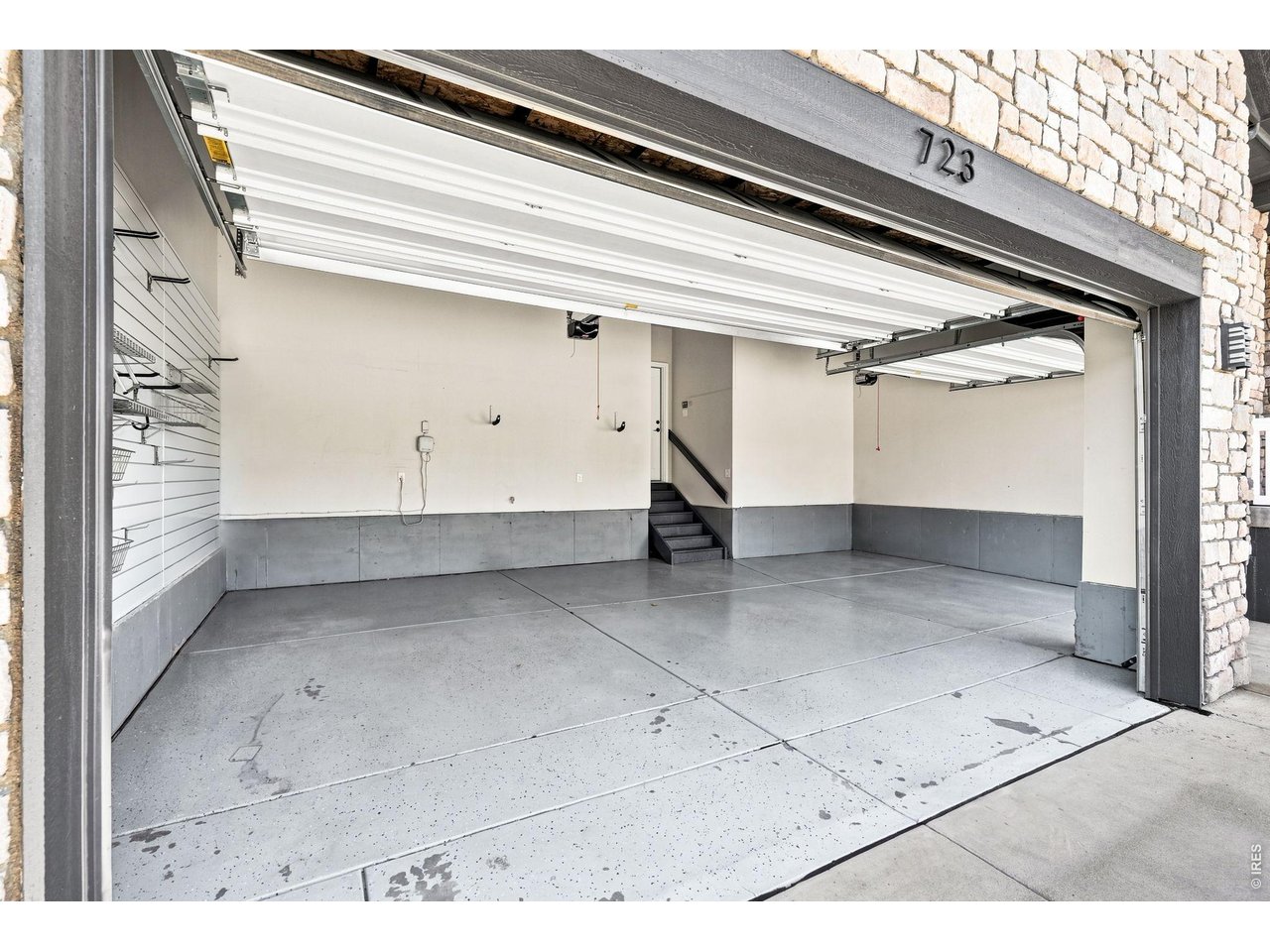 Empty two-car garage with open overhead doors, concrete floor, wall storage racks, and steps into the home.