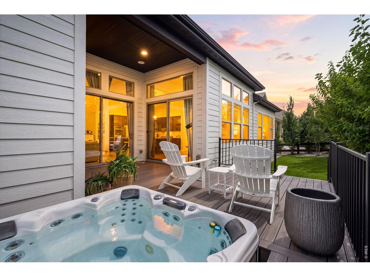 Hot tub and Adirondack chairs on a wood deck beside a modern home at dusk.