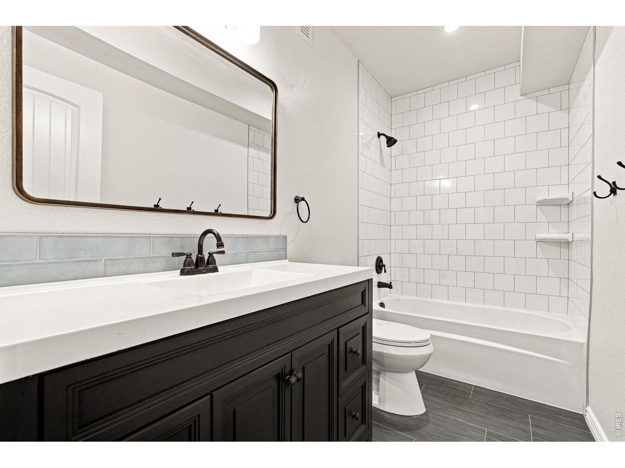 Bathroom with dark paneled vanity, large mirror, and white subway-tile tub and shower.