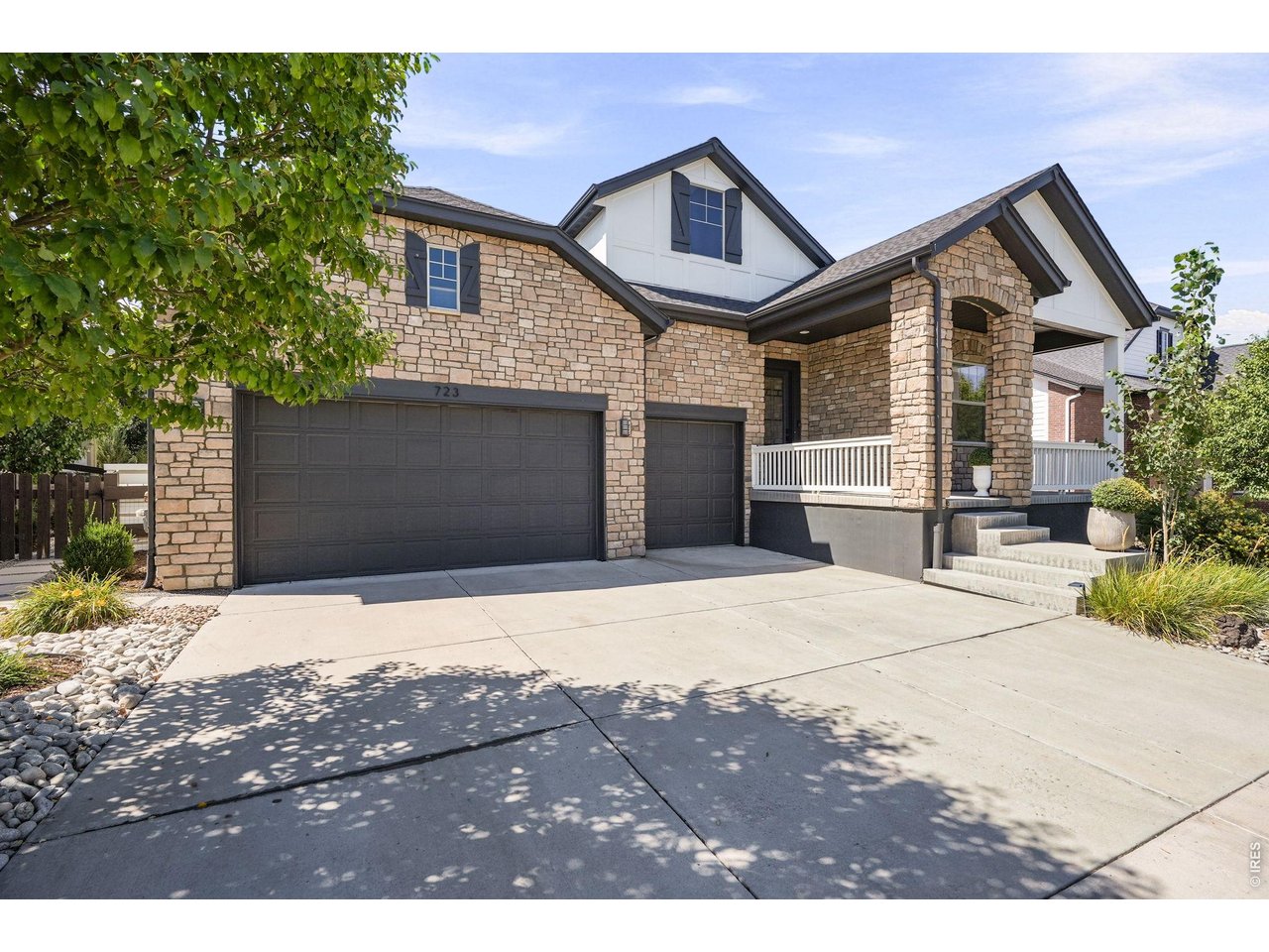 Stone-fronted two-story home with dark double garage doors, covered porch, and broad driveway.
