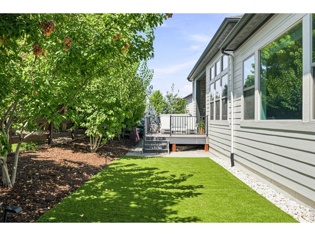 Backyard with a small deck, bright green lawn, and mature leafy trees beside the home.