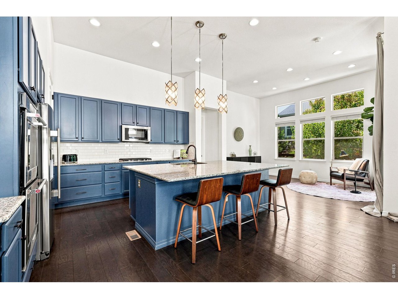 Open kitchen with blue cabinets, granite island, stainless steel appliances, and pendant lights.