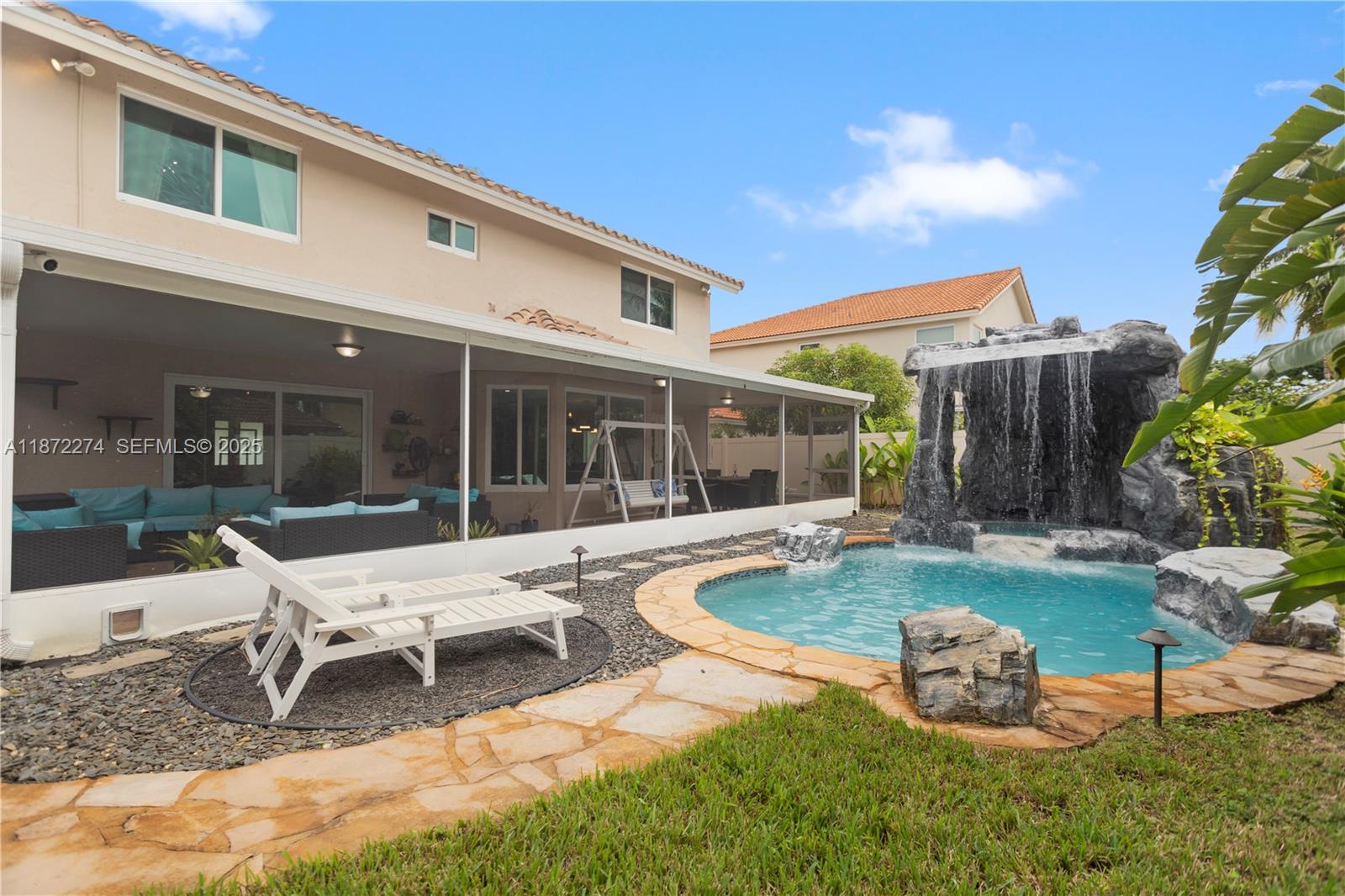 Backyard pool with a dramatic rock waterfall beside a home and screened patio.