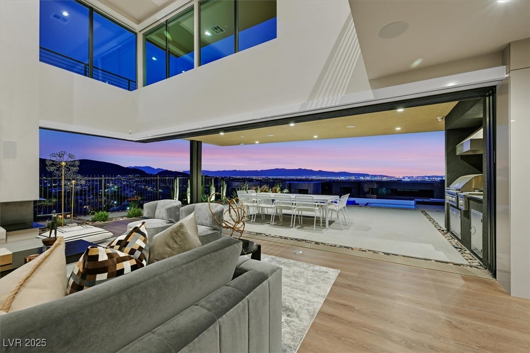 Modern living room opening to a terrace with a pool and city-and-mountain views at dusk.