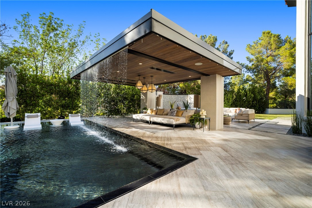 Modern covered patio with cream lounge seating beside a reflecting pool and cascading water.