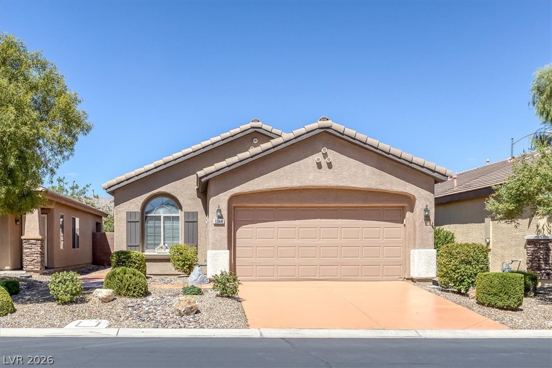 Single-story stucco home with a two-car garage, arched window, and desert landscaping.