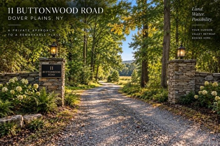 Gravel driveway entrance framed by stone pillars, lanterns, and leafy trees.