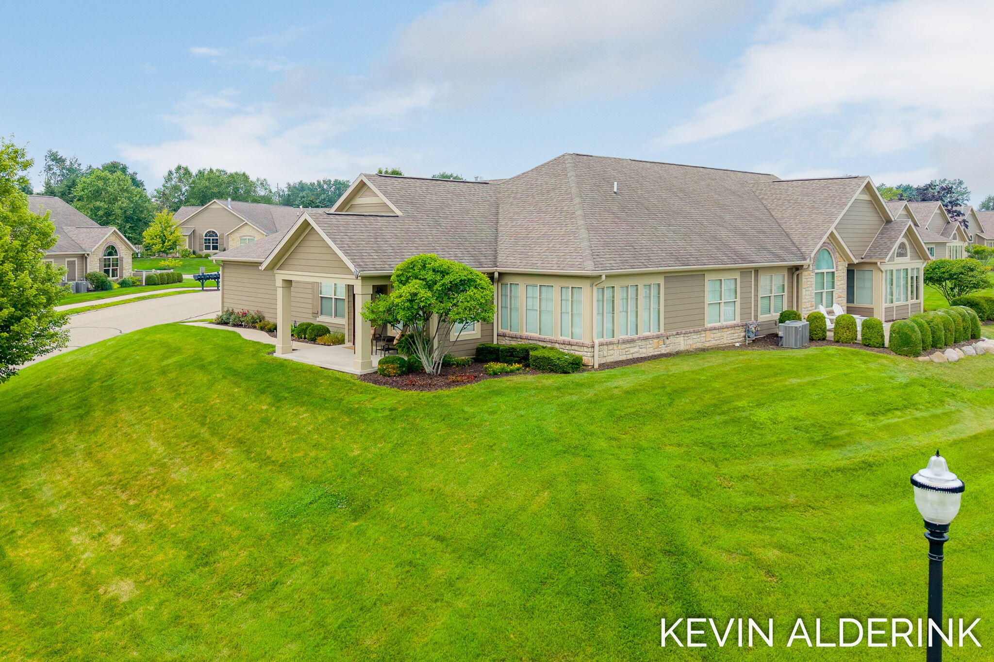 Single-story beige home with a stone base, covered entrance, and broad green lawn.