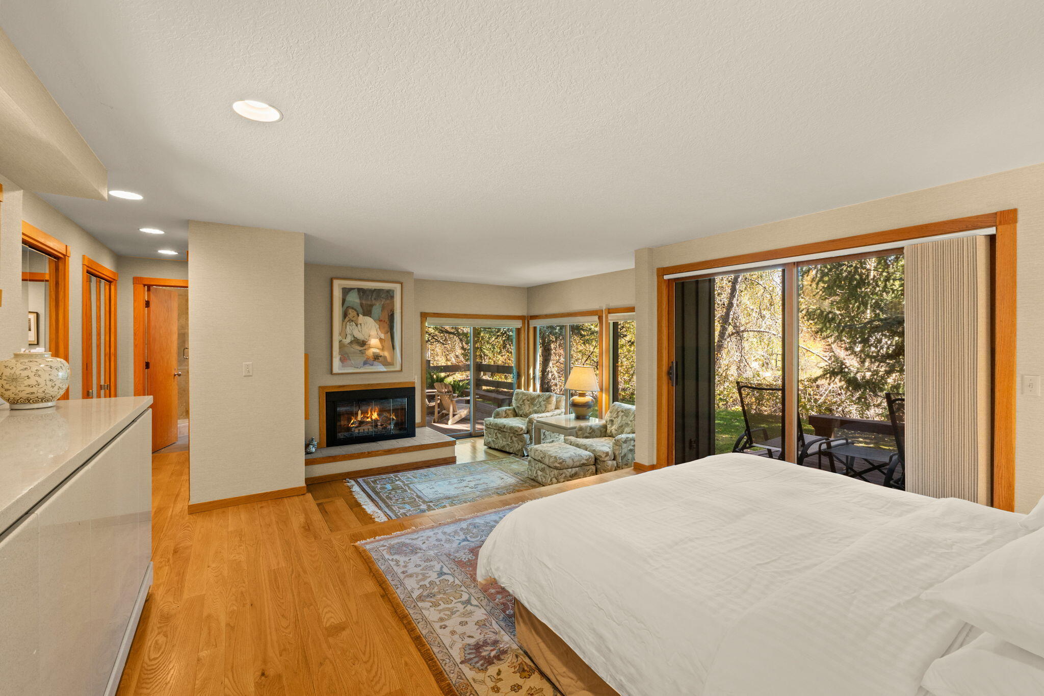 Bedroom with a fireplace, sitting area, and sliding doors opening onto a leafy patio.