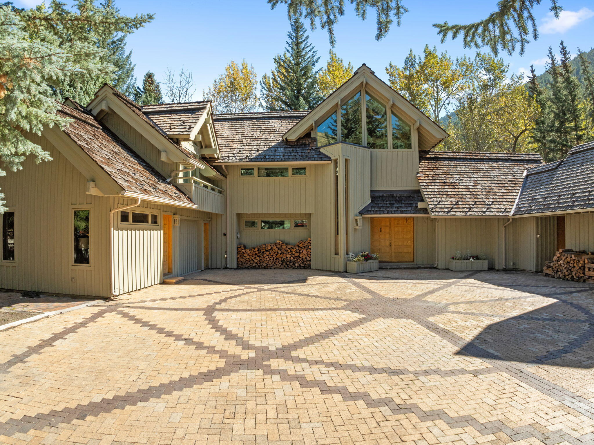 Mountain-style home with cedar-shingle roofs and tall gabled windows overlooking a patterned brick courtyard.