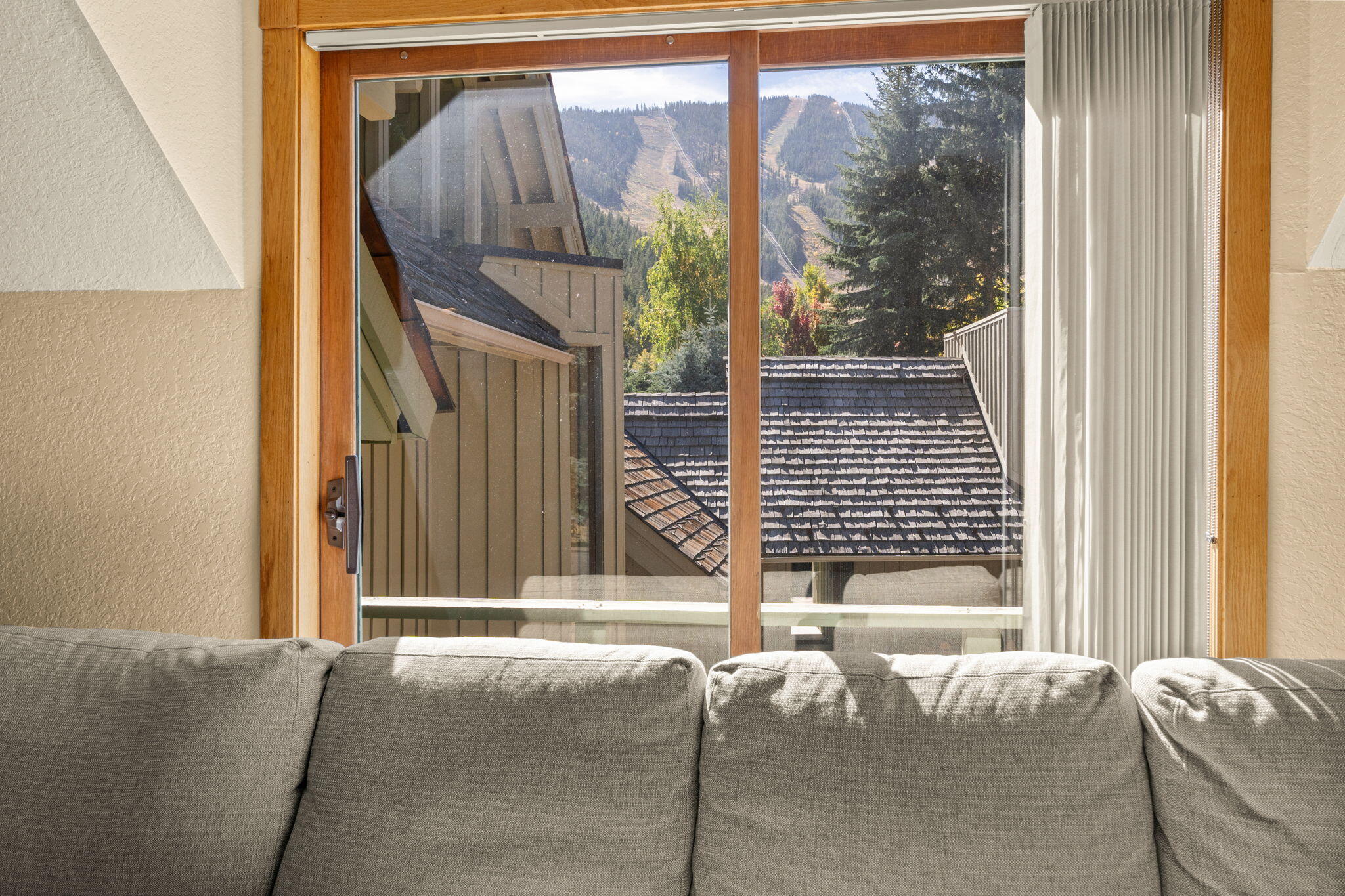 Living room with a gray sofa and large window overlooking mountains and ski trails.