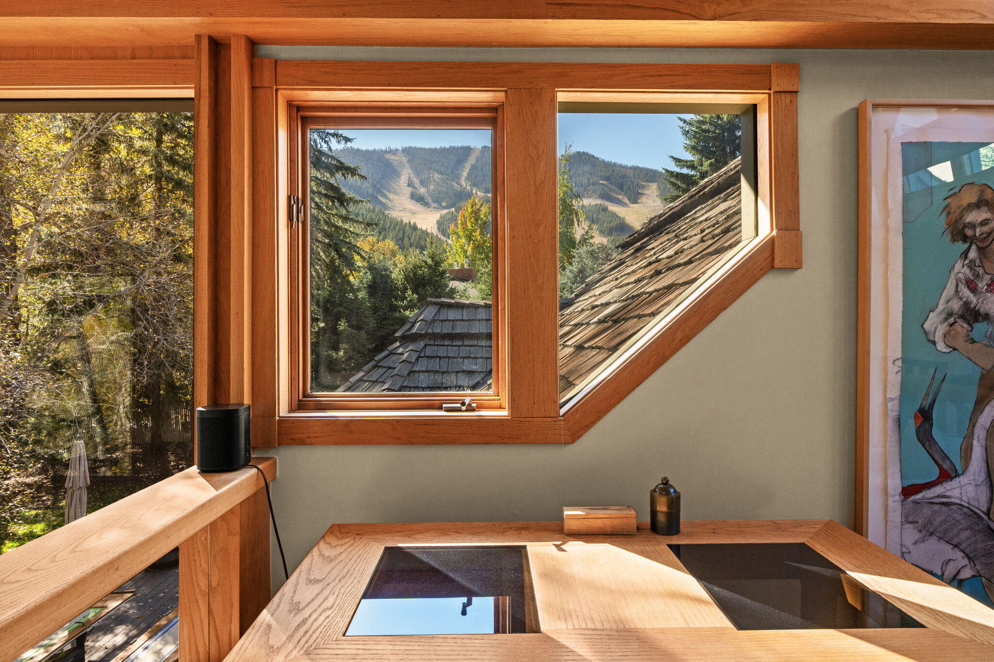 Wood-trimmed interior with angled windows framing a mountain view and evergreen trees.