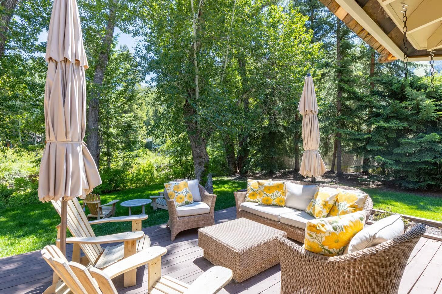 Furnished deck with wicker seating and yellow floral cushions, shaded by mature trees.