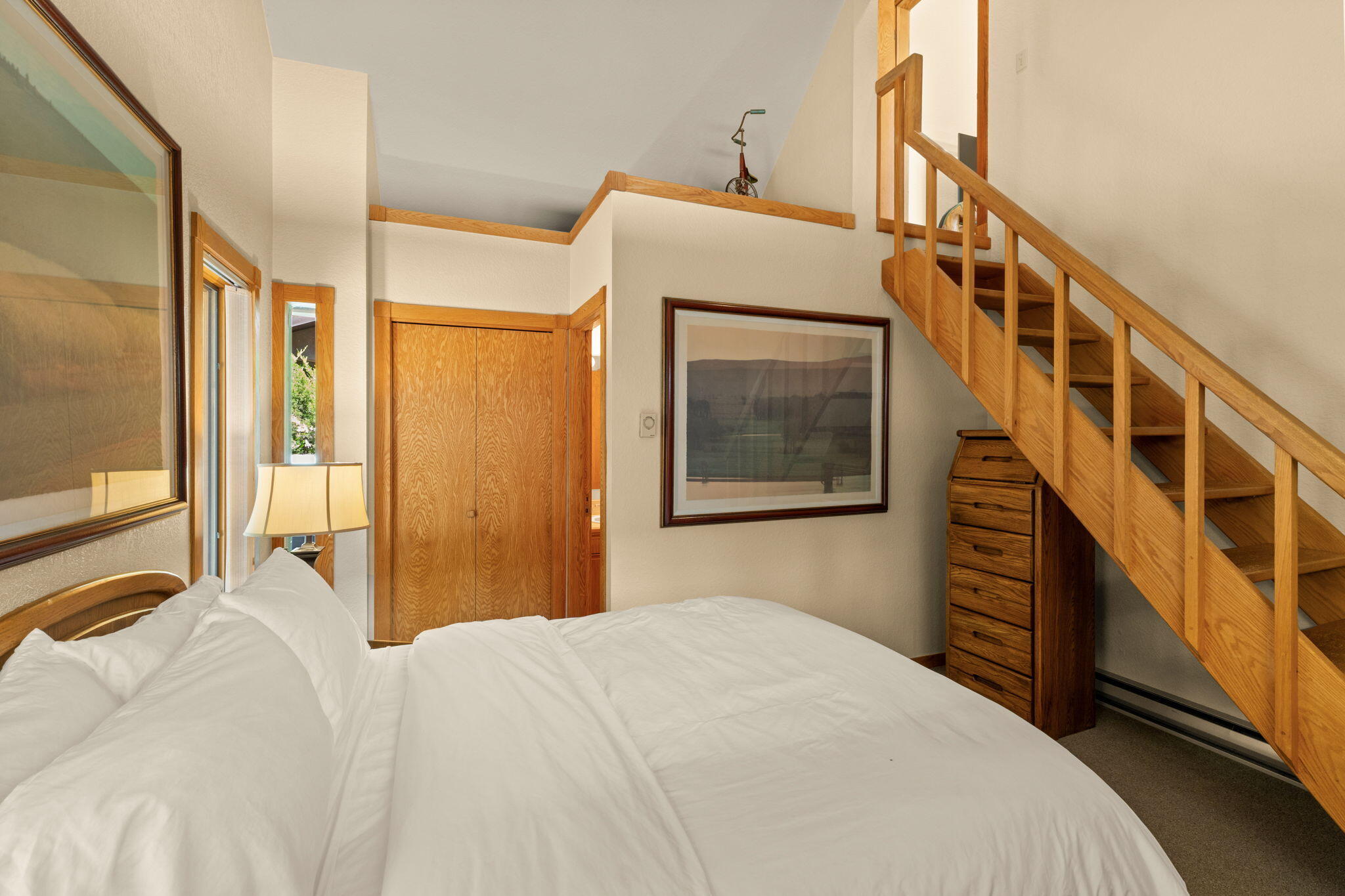 Bedroom with a white bed and wooden staircase leading to a loft.