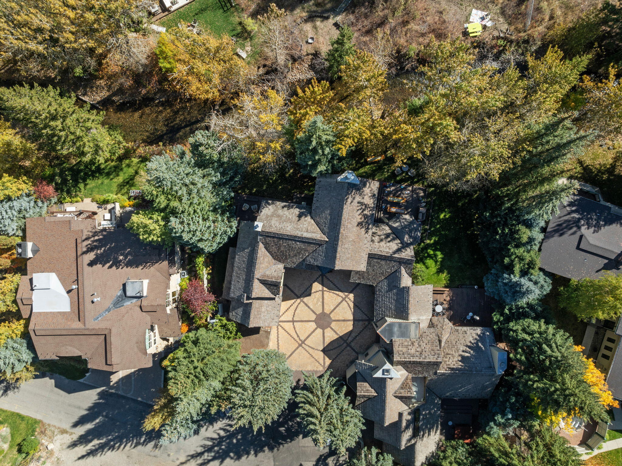 Aerial view of a shingled home and geometric courtyard surrounded by autumn trees.