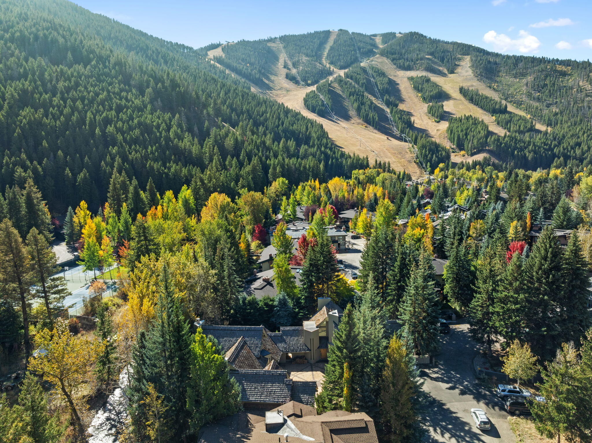 Aerial view of a wooded neighborhood beneath a mountain with ski runs and autumn foliage.