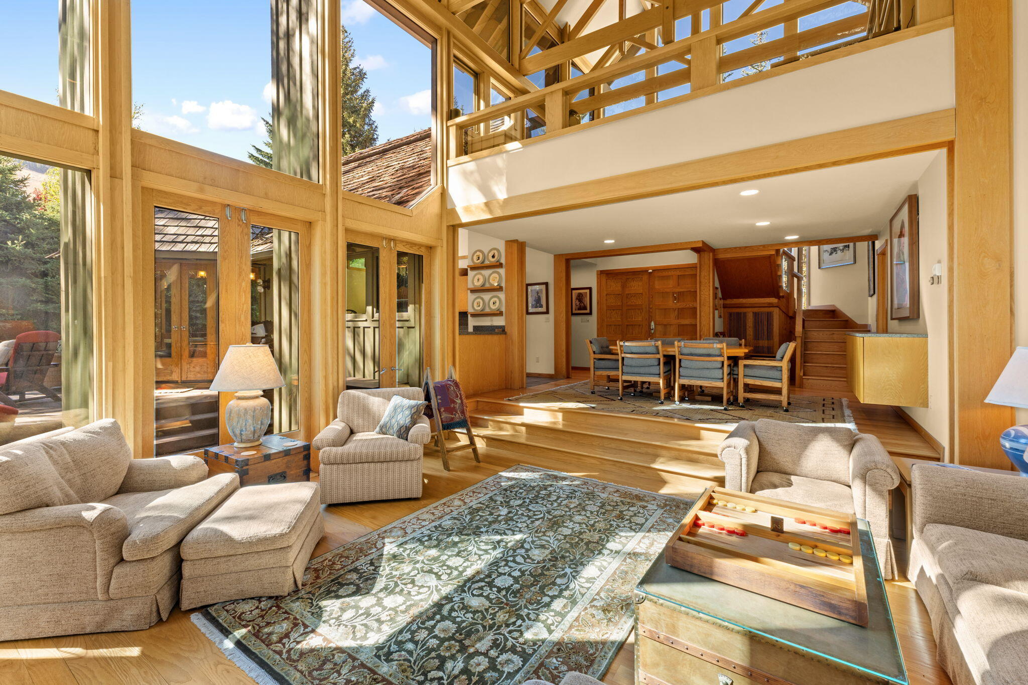 Furnished great room with tall windows, exposed timber beams, and a raised dining area.