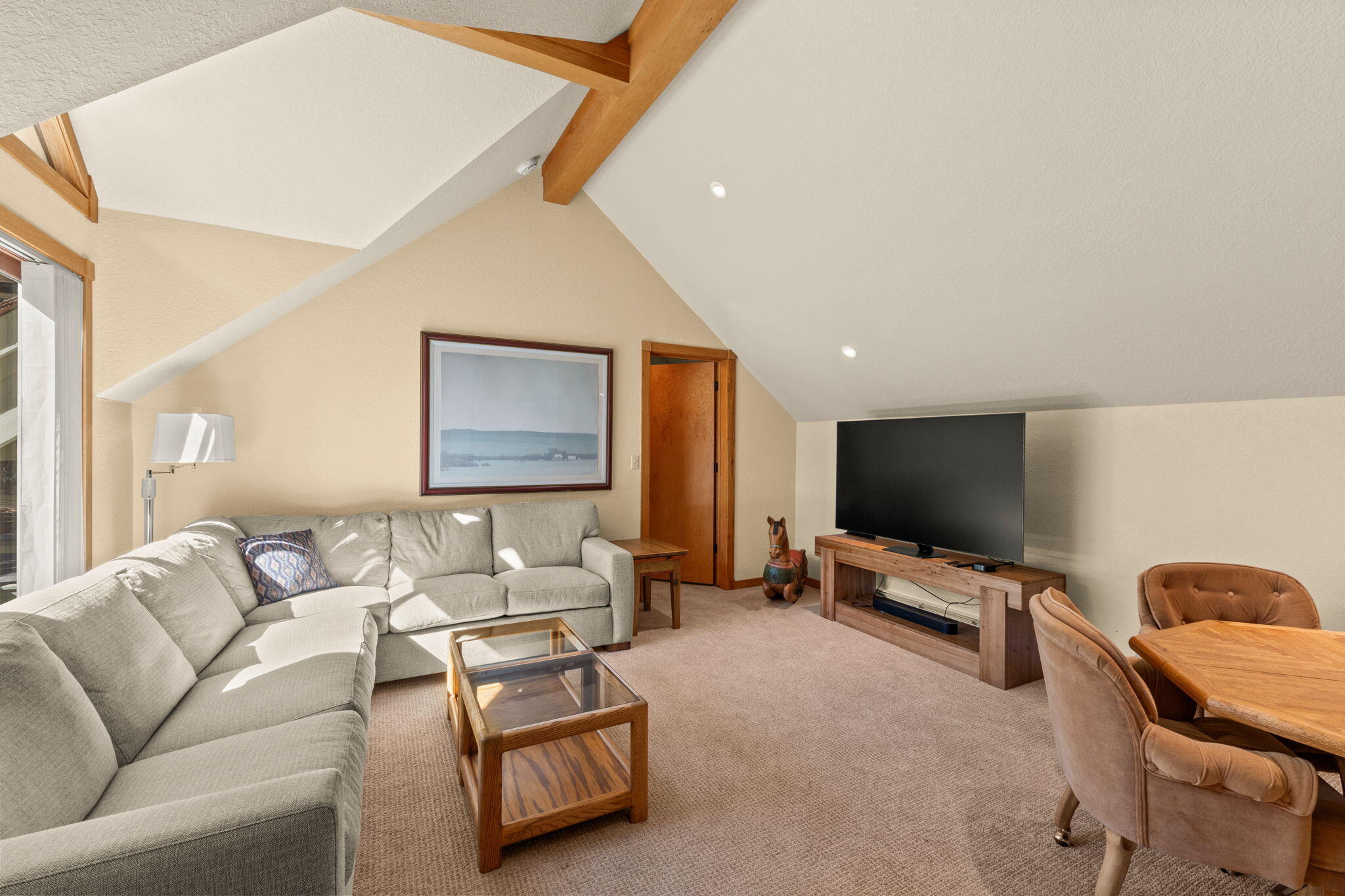 Vaulted living room with exposed wood beams, a gray sectional, and a TV console.