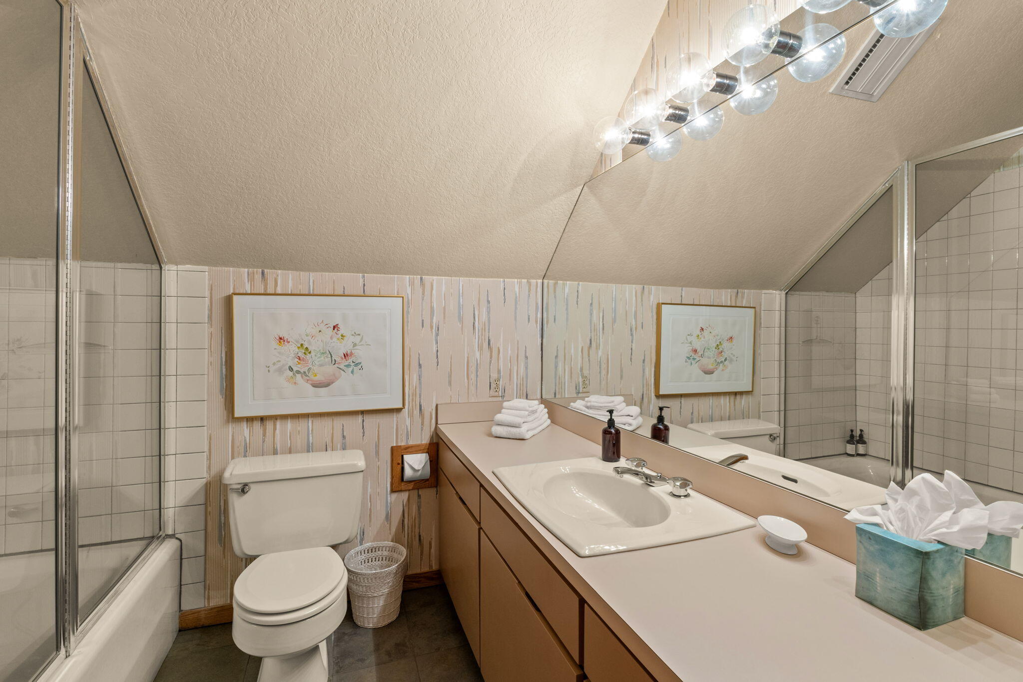 Bathroom with a long vanity, mirrored wall, glass-enclosed tub and shower, and sloped ceiling.