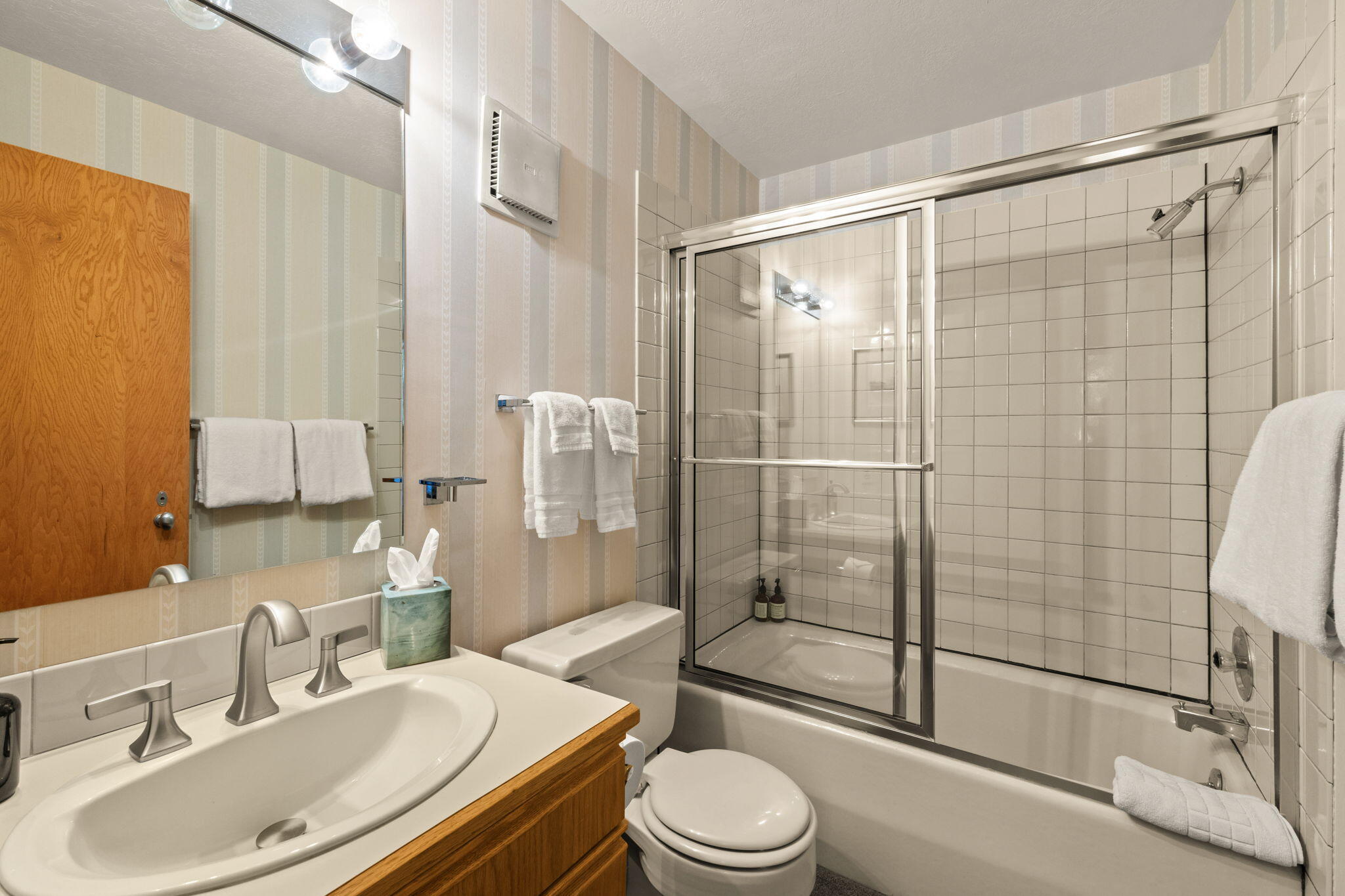 Bathroom with a wood vanity, oval sink, and tiled tub-shower behind sliding glass doors.