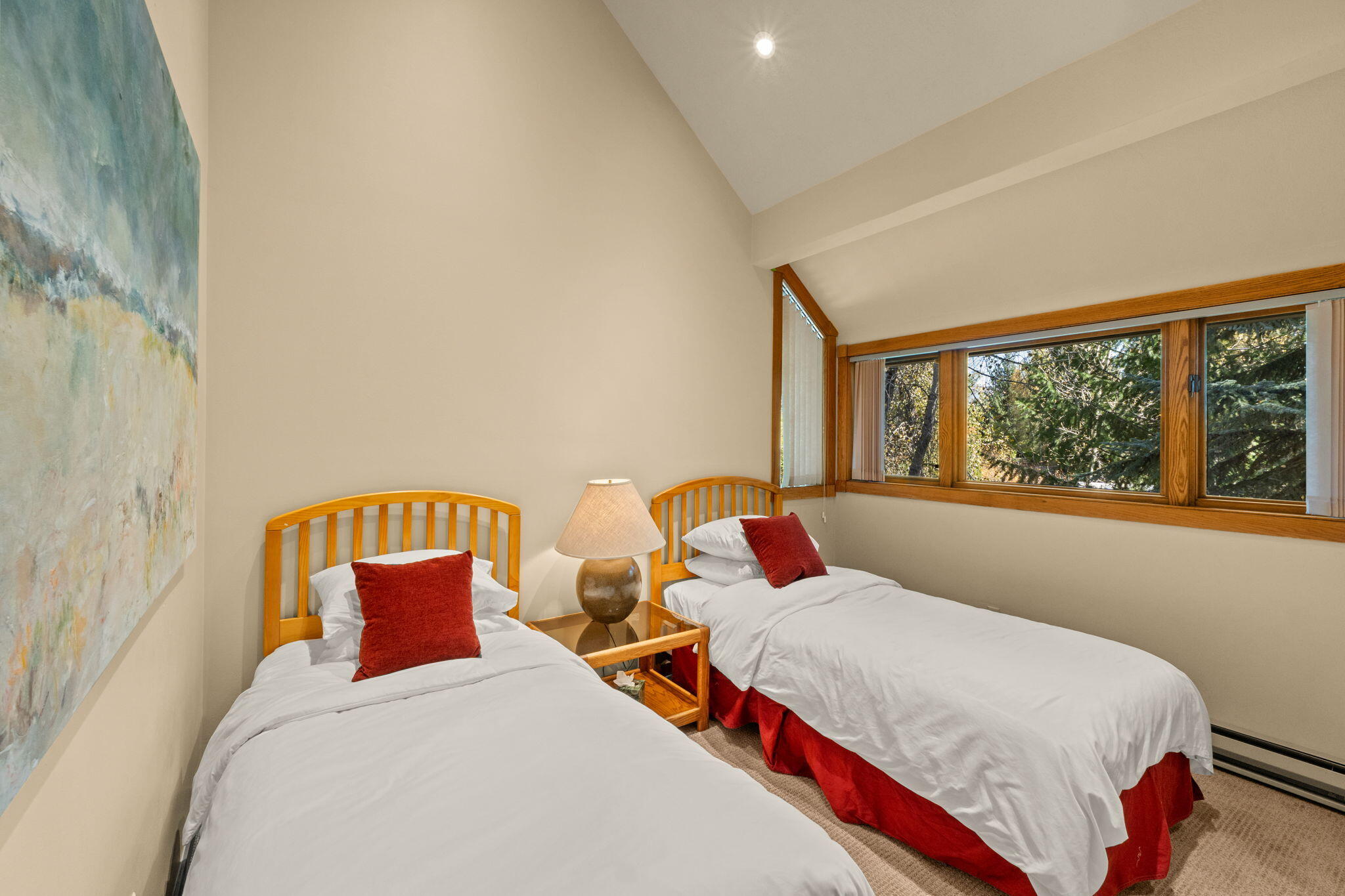 Bedroom with two twin beds, red accents, and large windows overlooking trees.