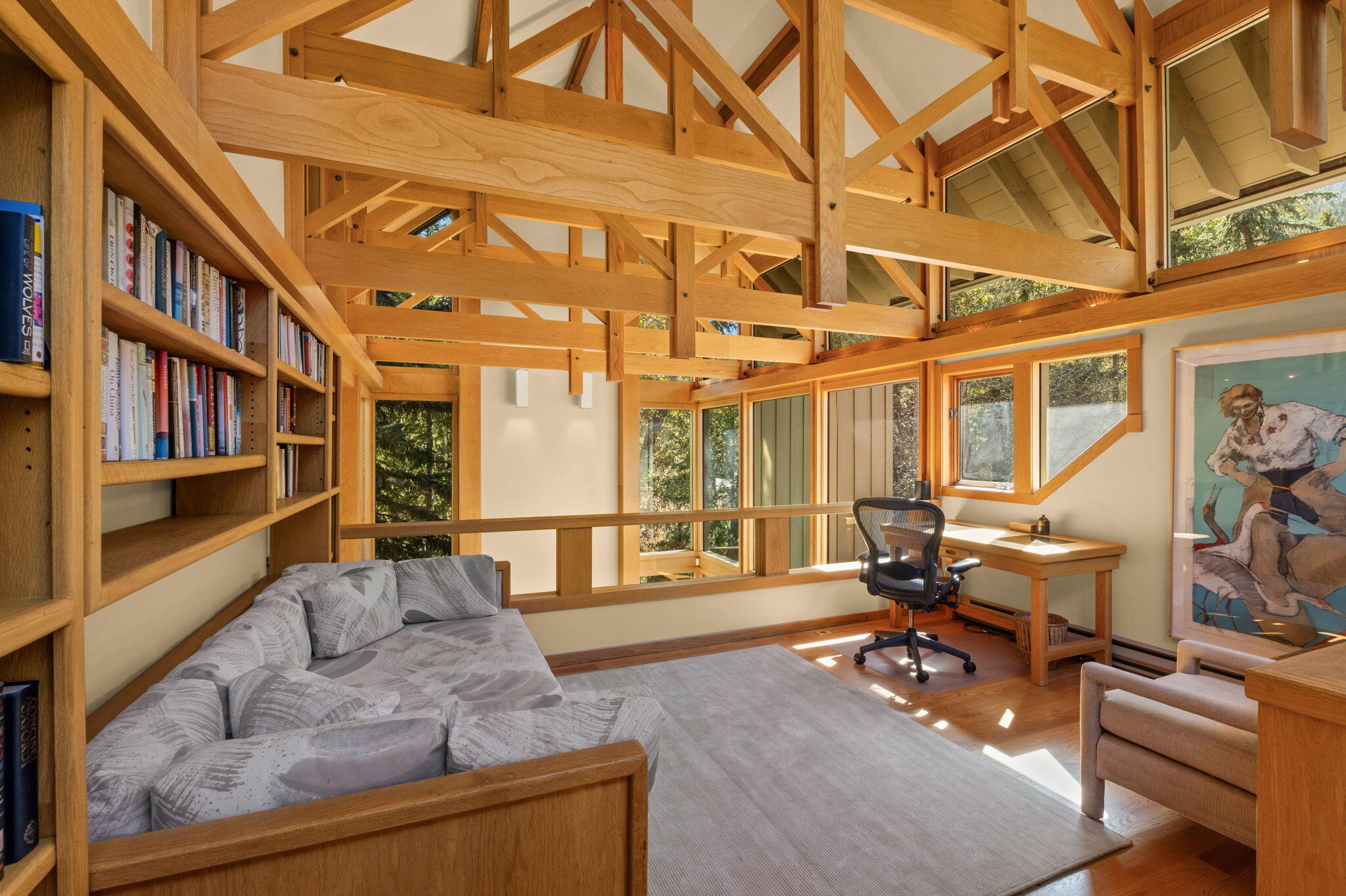 Living room and workspace with exposed timber trusses, built-in bookshelves, and large windows.