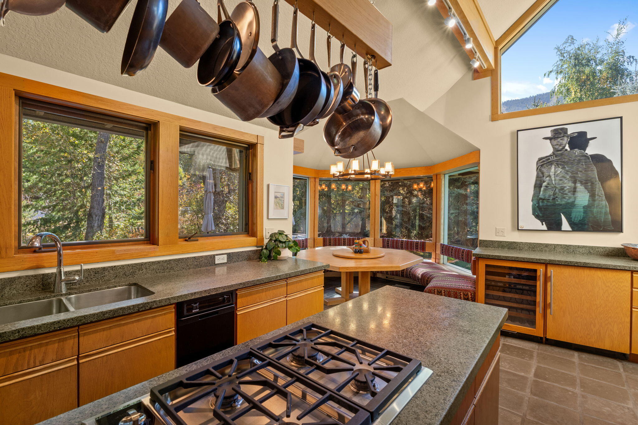 Kitchen with wood cabinetry, a large gas cooktop island, hanging pans, and a windowed breakfast nook.