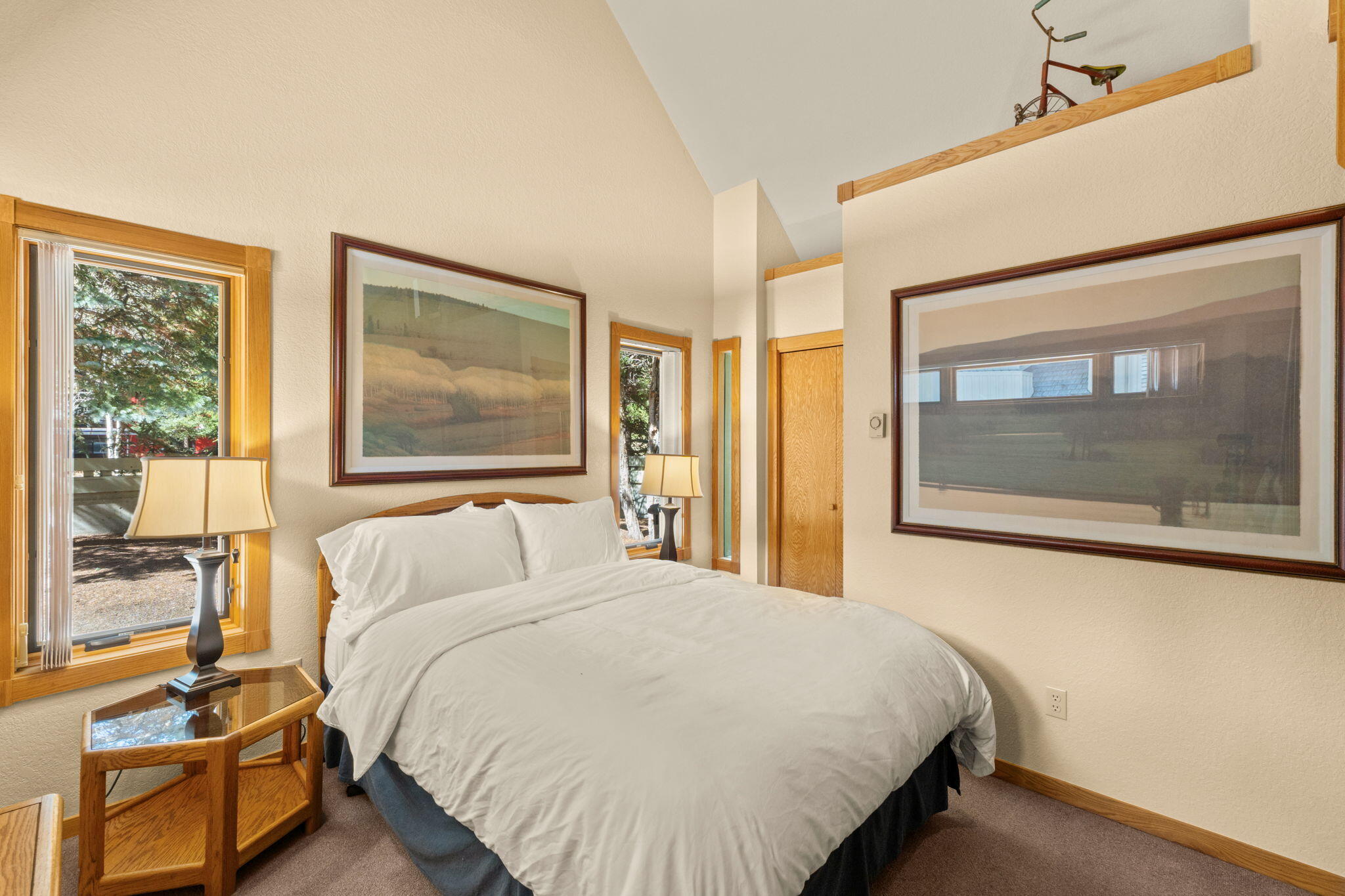 Bedroom with a white bed, warm wood trim, large framed artwork, and a high ceiling.