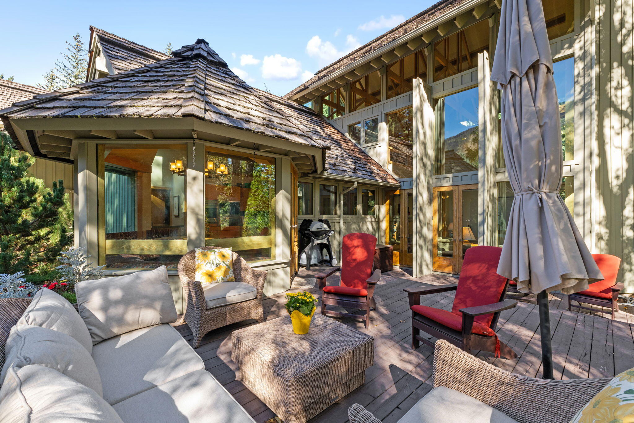 Furnished outdoor deck with wicker seating, red Adirondack chairs, and a grill beside the home.