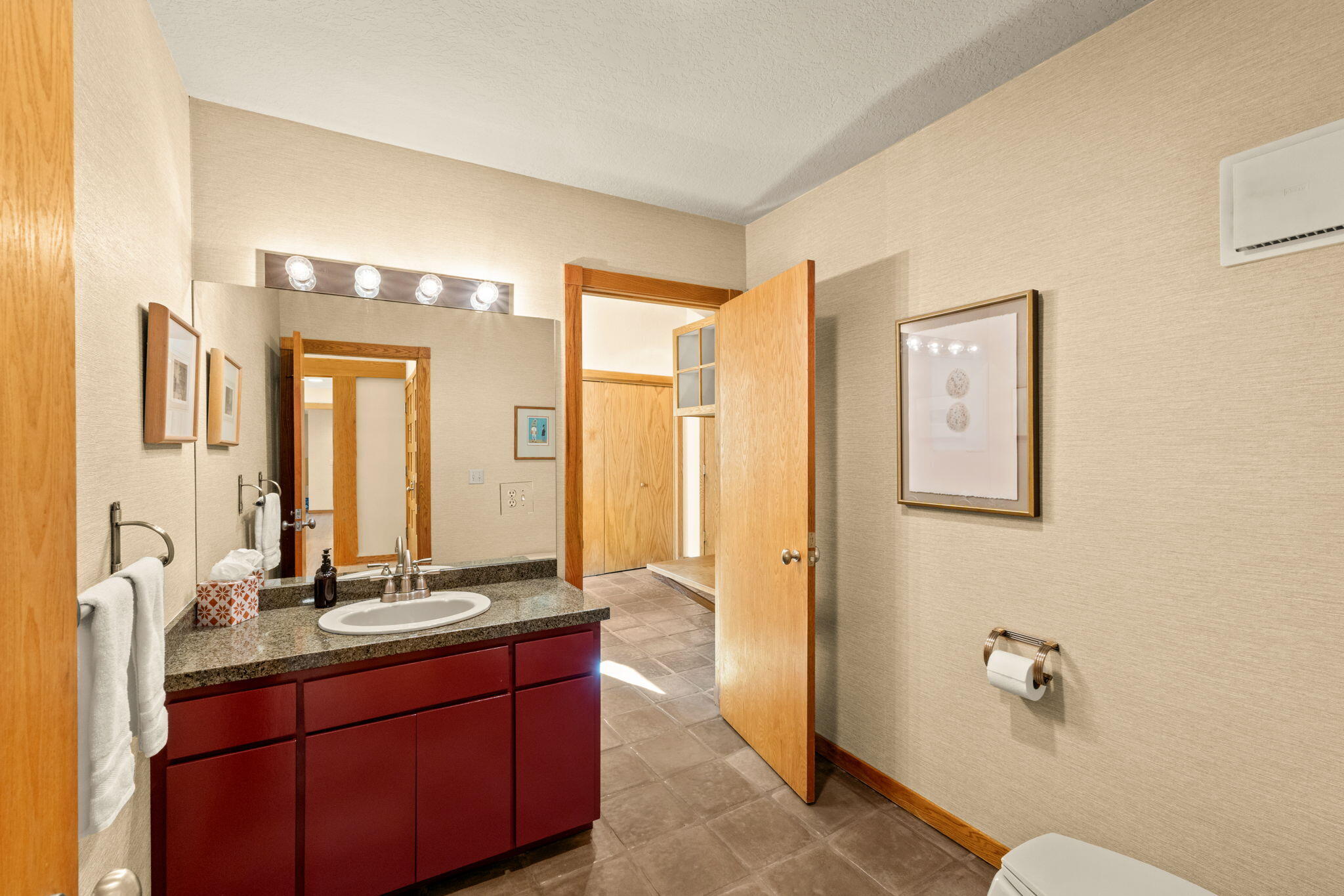Bathroom with a red-brown vanity, stone countertop, and open wooden door to a tiled area.
