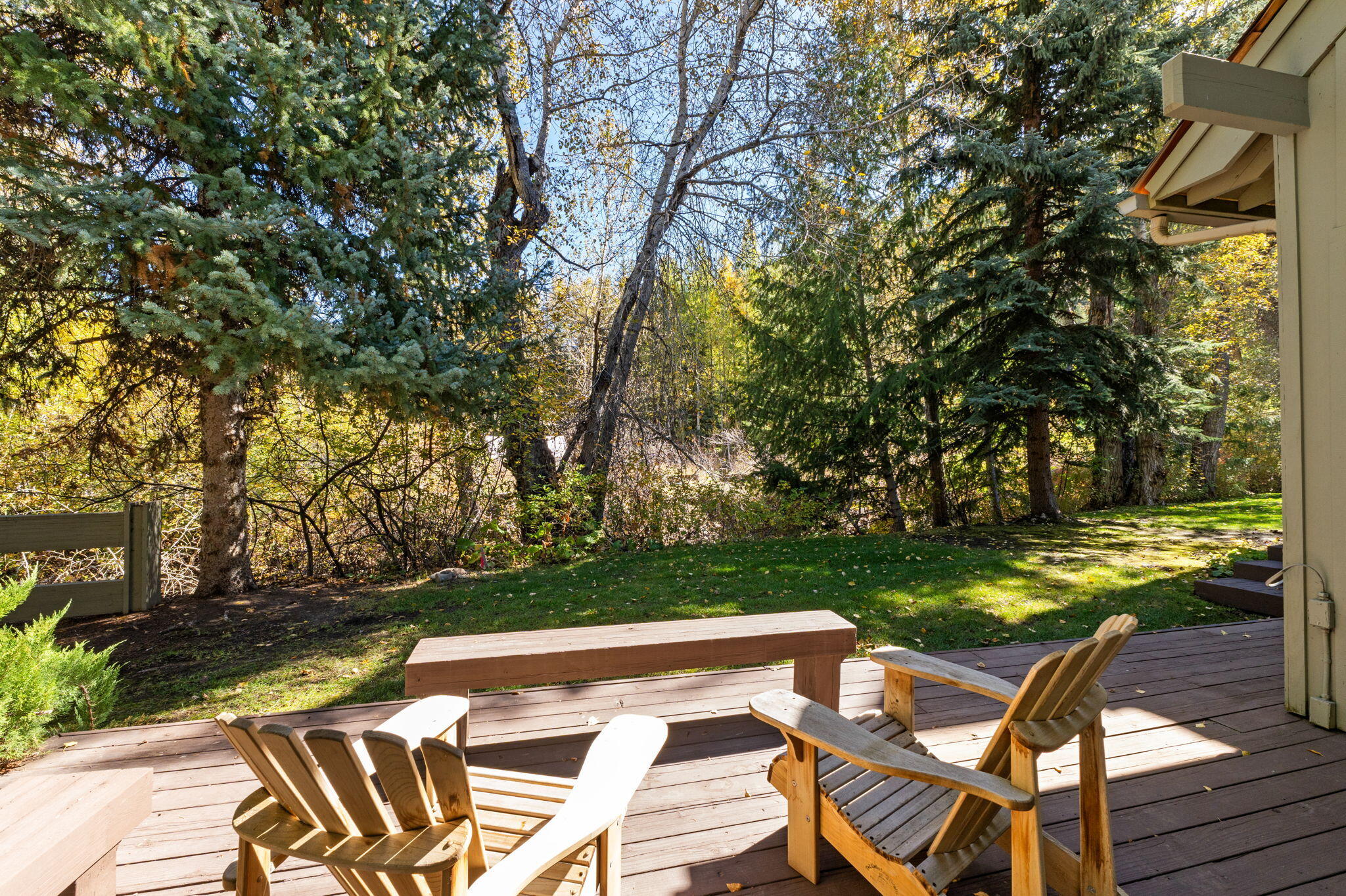 Wooden deck with Adirondack chairs overlooking a lawn and wooded backyard.