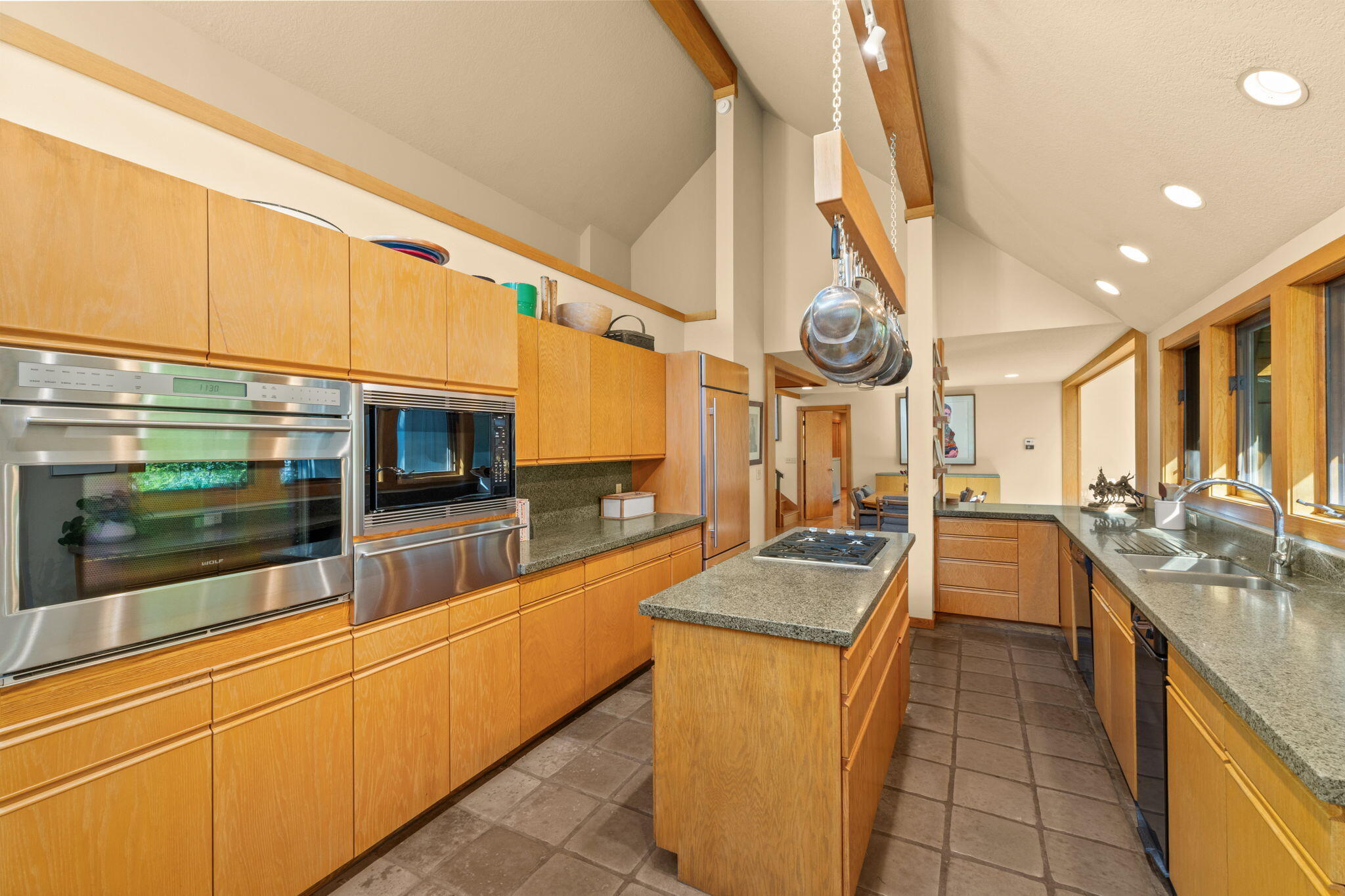 Kitchen with honey-colored wood cabinets, granite counters, a cooktop island, and large windows.