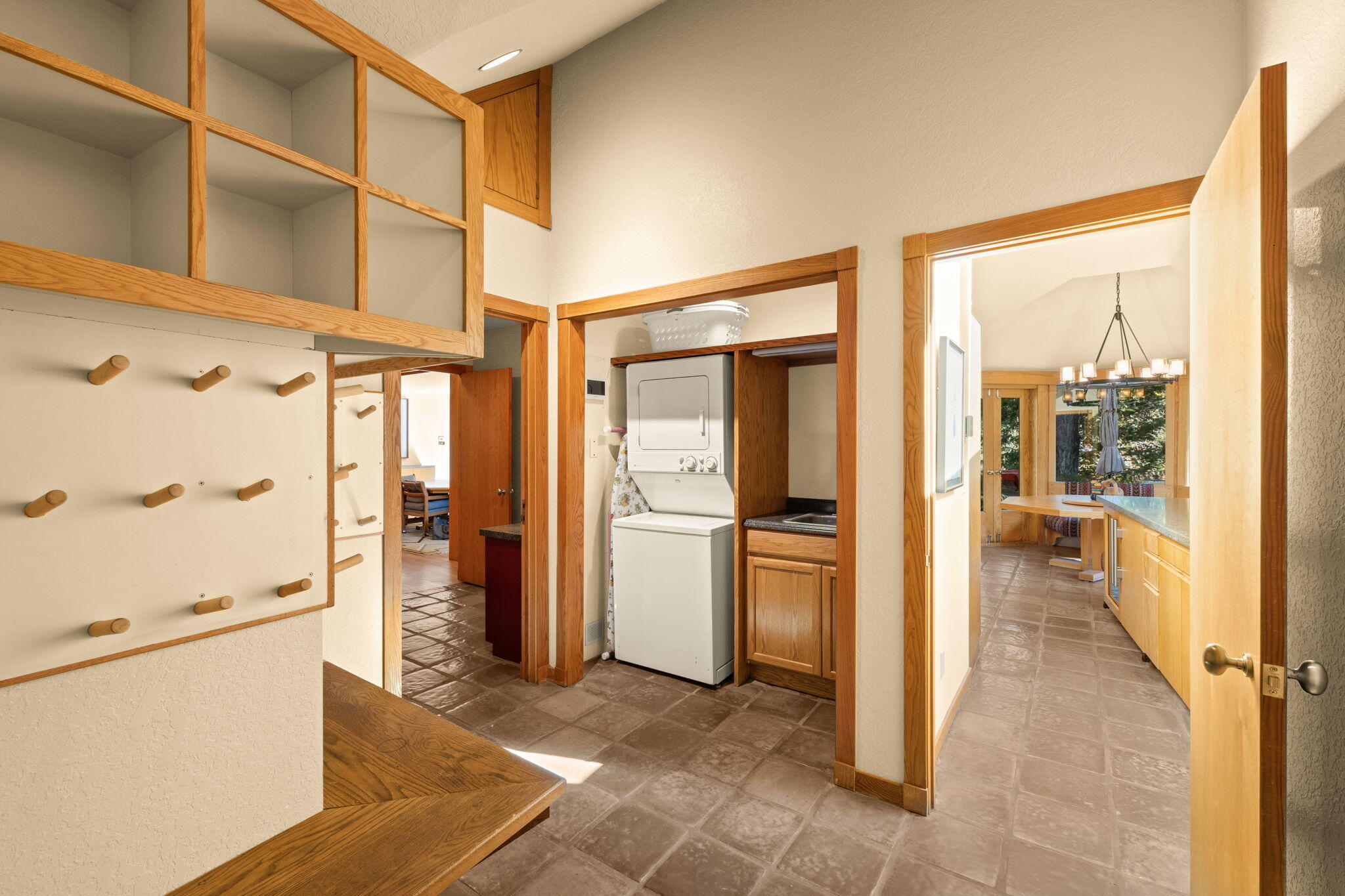 Laundry room with built-in wooden cubbies and hooks, a stacked washer and dryer, and tile flooring.