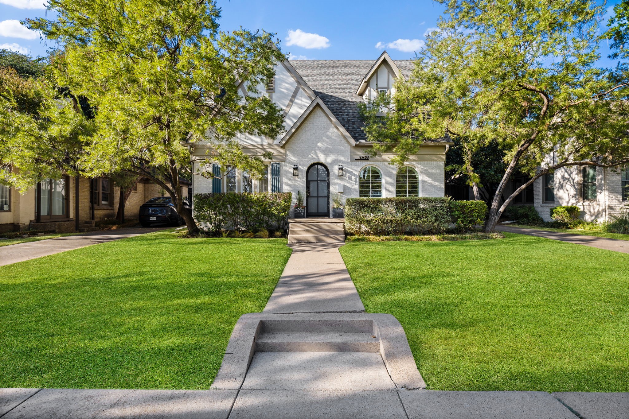 White brick home with steep gables, arched windows, and a walkway through the front lawn.