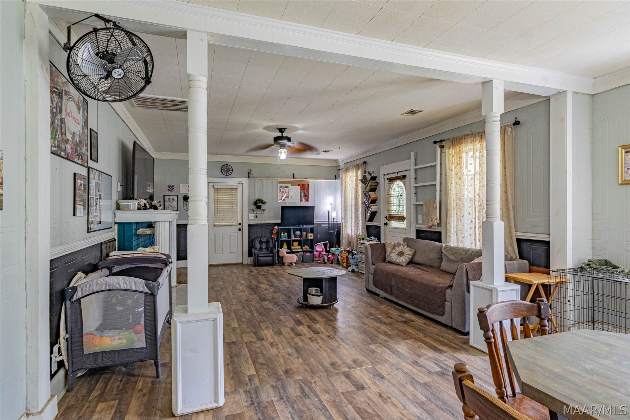 Living room with white columns, wood-look floors, a gray sofa, and children’s toys.