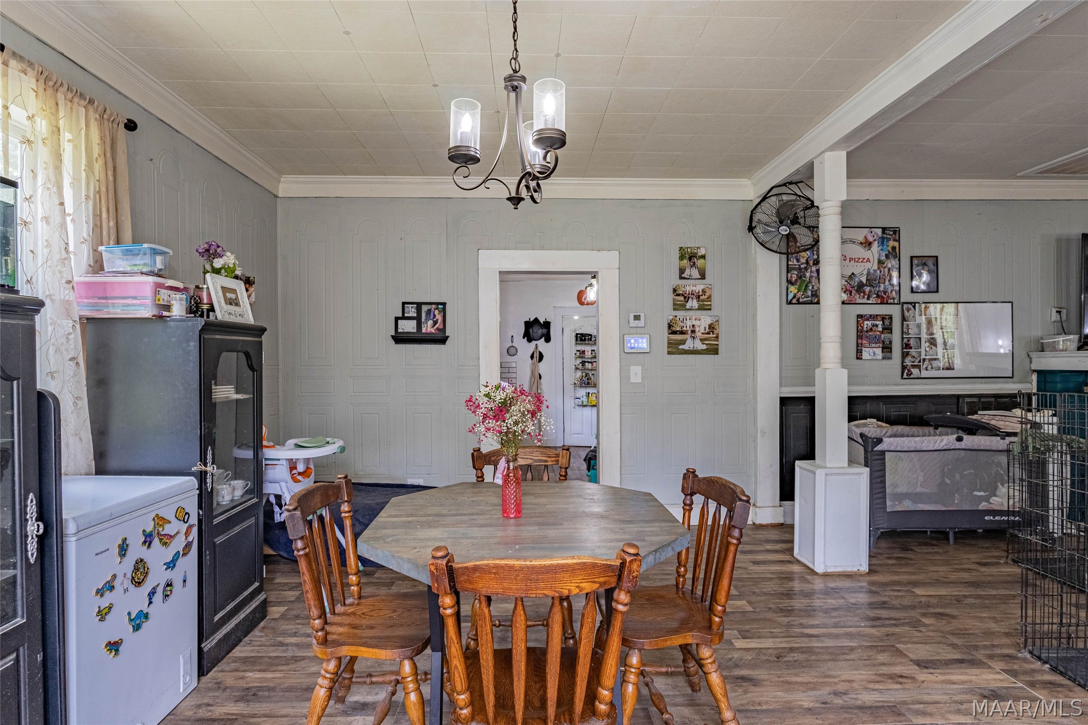 Dining room with a wooden table, chandelier, paneled walls, and an adjoining area with a crib.