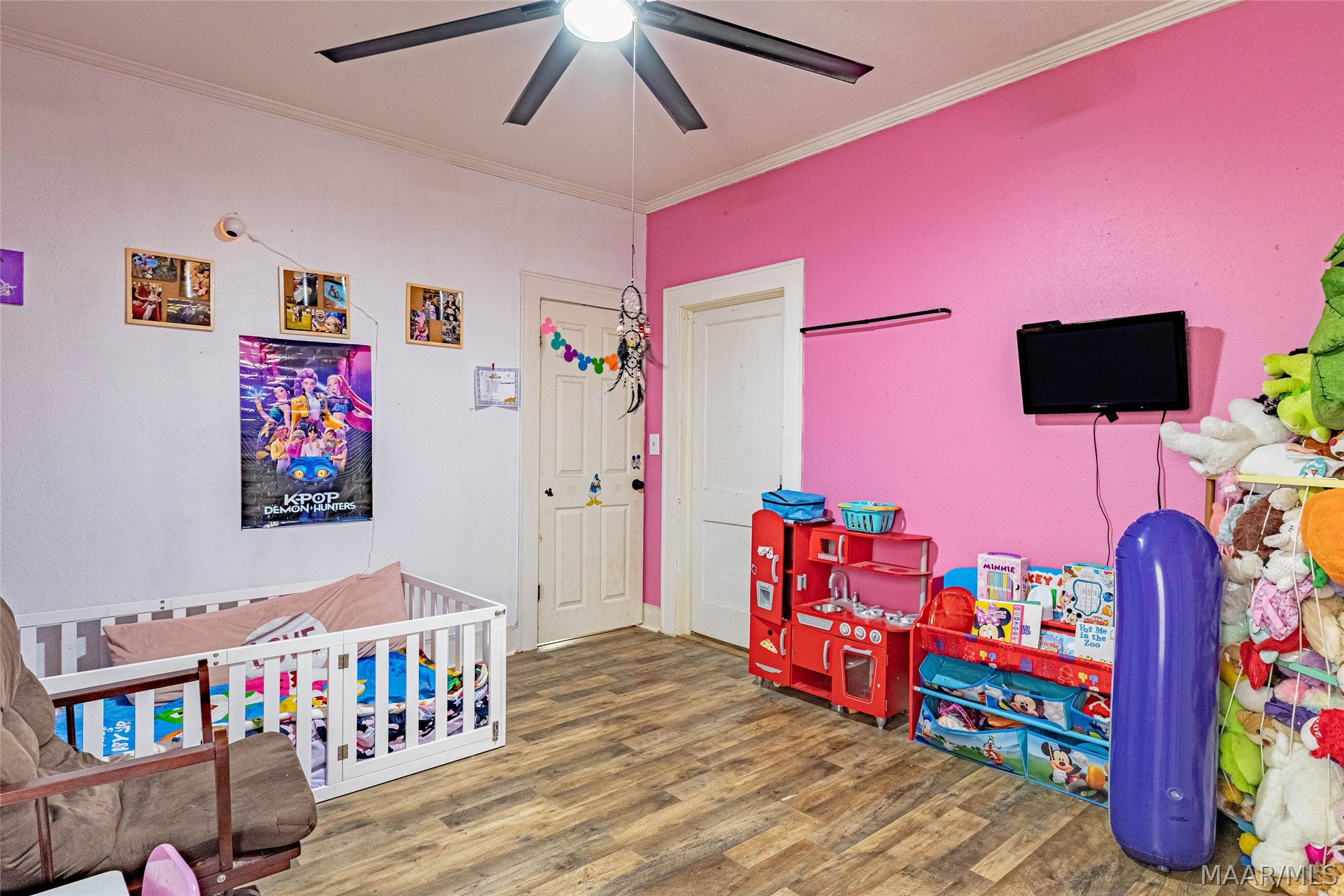 Child's bedroom with a white crib, bright pink wall, toy kitchen, and shelves of toys.