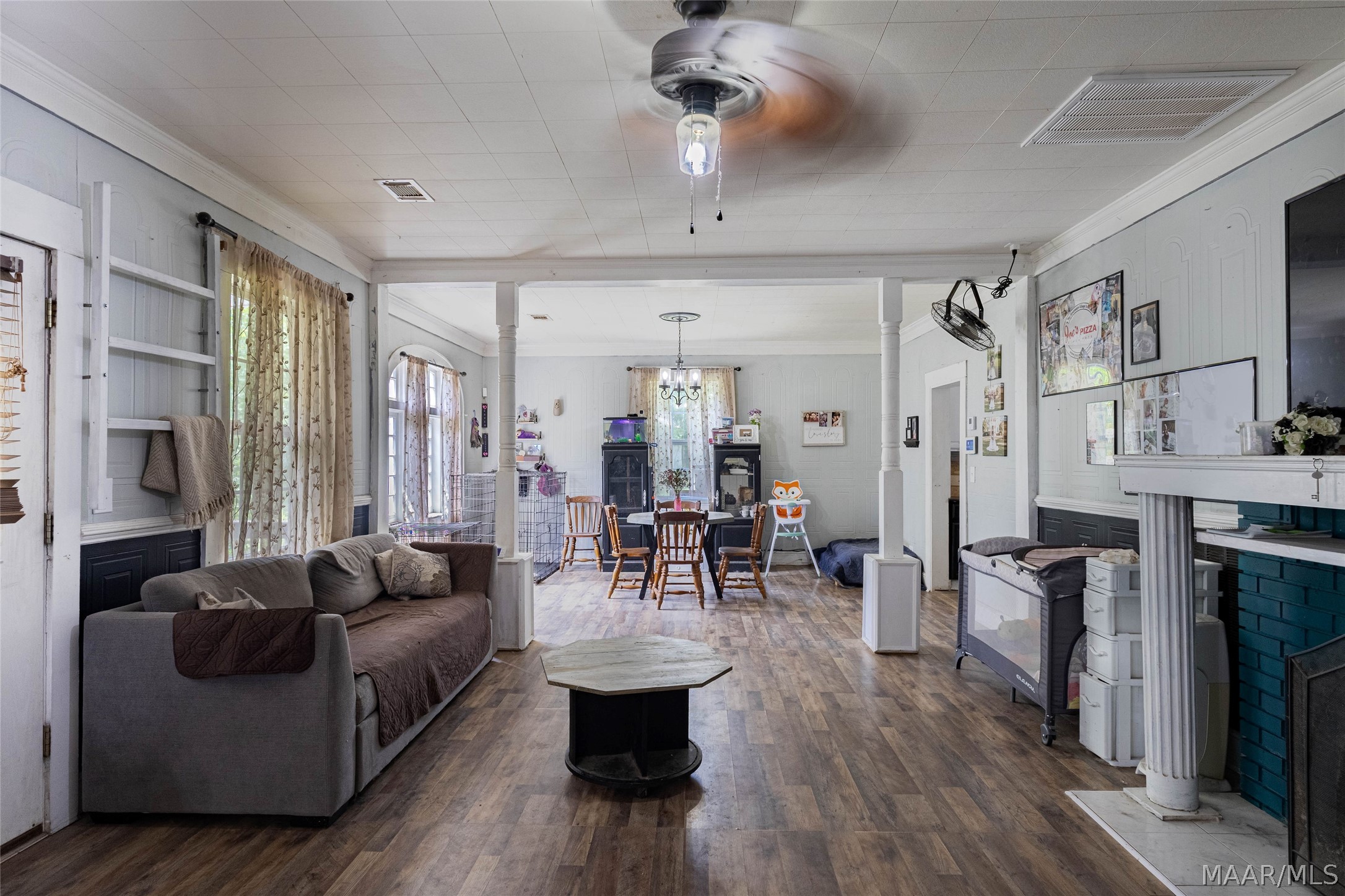 Living room with a gray sofa, wood-look floors, white columns, and a teal-brick fireplace.
