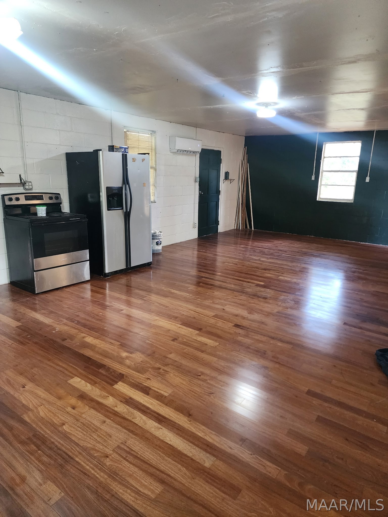 Open kitchen and living area with polished hardwood floors, a stove, refrigerator, and dark accent wall.