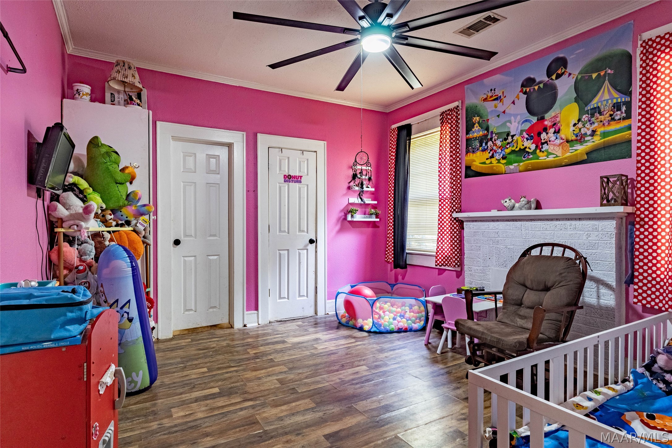 Pink child's bedroom with a white crib, rocking chair, colorful ball pit, and stuffed animals.